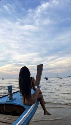 a woman sitting on top of a blue boat in the ocean next to shore line