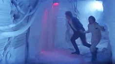 two people are walking through an ice cave with snow on the ground and lights in the background