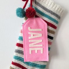 a pink name tag hanging from the side of a striped sock with pom - poms