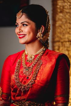 a woman in red is smiling and wearing gold jewelry on her head, with an elaborate necklace