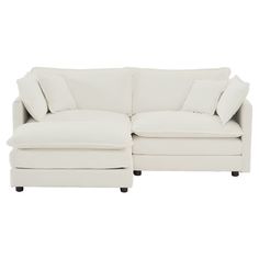 a white sectional couch with pillows on it's back and foot rests against the wall