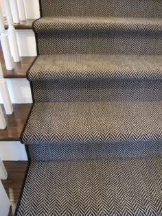 a carpeted staircase with white handrails and black chevron rug on the bottom