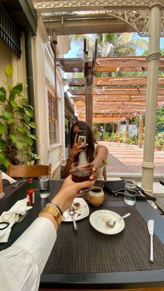 two people sitting at a table with food and drinks in front of them, taking pictures