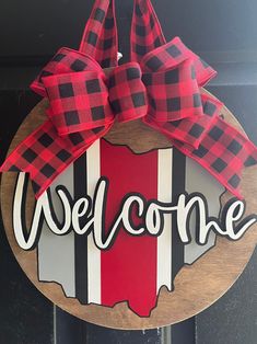 a welcome sign with a red and black checkered bow hanging on the front door