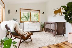 a baby's room with a crib, rocking chair, dresser and potted plant