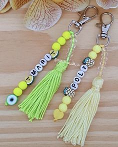 two key chains with beads and tassels on top of a wooden table next to flowers