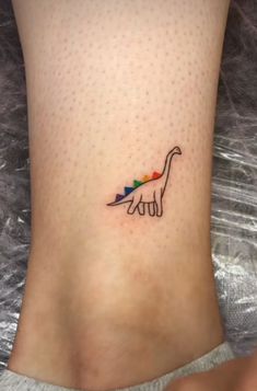 a small tattoo on the ankle of a woman's foot with a colorful dinosaur