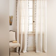 a white chair sitting in front of a window next to a curtain with pom - poms on it