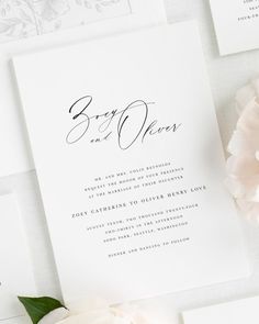 the wedding stationery is laid out on top of each other, with white flowers and greenery