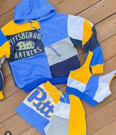 a blue and yellow hoodie with matching shorts is laying on a wooden floor next to shoes