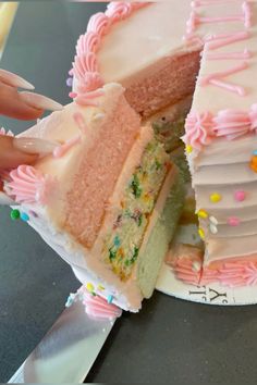 a person is holding a knife and cutting a piece of cake with pink frosting