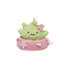 a green stuffed animal sitting in a pink bowl with a flower on it's head