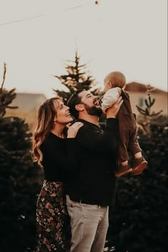 a man and woman holding a baby while standing in front of a christmas tree lot