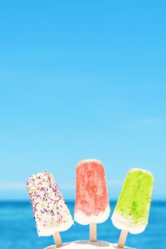 three popsicles sitting on top of each other in front of the ocean with sprinkles