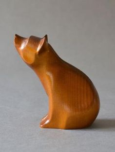 a small wooden cat figurine sitting on top of a white surface with its head turned to the side