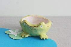 a green frog planter sitting on top of a blue table cloth next to a white flower