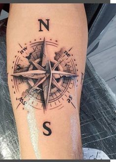 a man's leg with a compass tattoo on it and the letter s in black ink