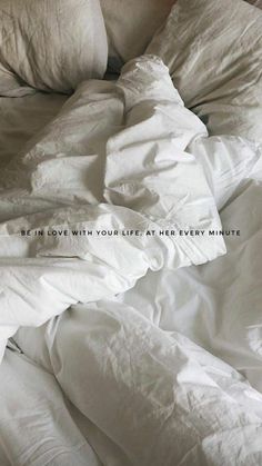 an unmade bed with white sheets and pillows that have the words be in love with your life at every minute