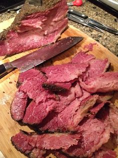 sliced up meat on a cutting board with a knife next to it and another piece of meat in the background