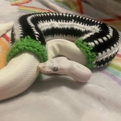 a white and black snake laying on top of a bed next to a stuffed animal