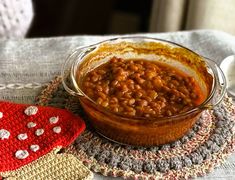 a bowl filled with beans sitting on top of a table next to a knitted mitt