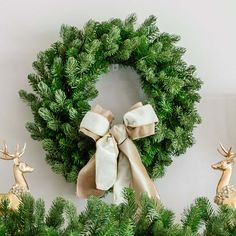 a christmas wreath with two deer figurines in front of it and one wearing a bow