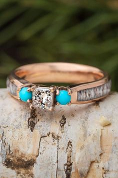 a close up of a ring on top of a tree branch with a diamond and turquoise stones