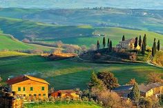 an italian countryside with rolling hills and houses in the foreground, surrounded by trees