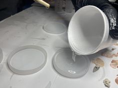 a person pouring water into a cup on top of a white table covered in seashells