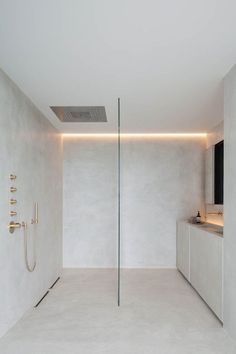 a bathroom with white walls and flooring next to a shower head mounted on the wall