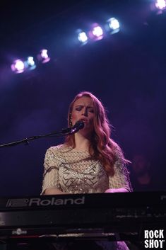 a woman standing in front of a keyboard on top of a stage with lights behind her