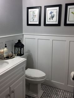 a white toilet sitting in a bathroom next to a sink and framed pictures on the wall