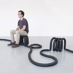 a man sitting on top of a chair next to black hoses in the floor