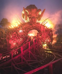 an amusement park at night lit up with red and yellow lights on the top of it