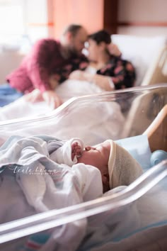 a baby is laying in a bed with his mother and father behind him on the other side