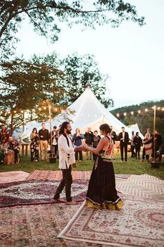 a man and woman dancing on a rug in the middle of a field with people standing around