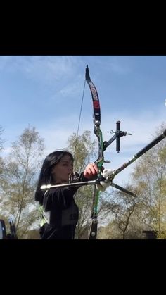 a woman holding onto a bow while standing in front of a car with an arrow on it