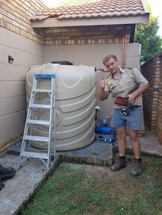 a man standing next to a water tank holding a drill and a tool in his hand