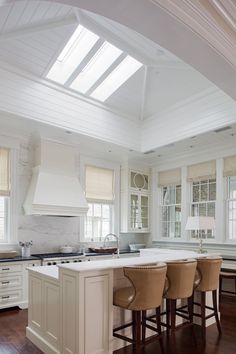 a kitchen with an island and four stools next to the counter top in front of two windows