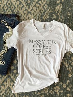 messy bun coffee scrubs t - shirt next to jeans on carpet with beaded necklace