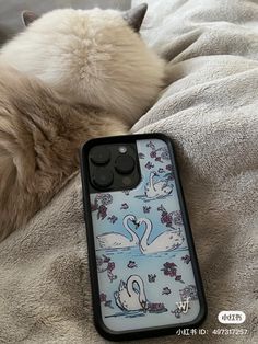 a cat laying on top of a bed next to a phone case with swans on it