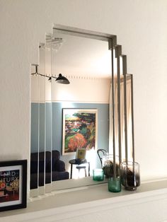 a mirror sitting on top of a white mantle next to a framed painting and vases