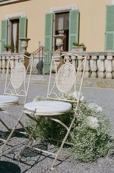 two white folding chairs sitting next to each other in front of a building with green shutters