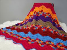 a crocheted blanket is on top of a white furnishing and it has multicolored stripes