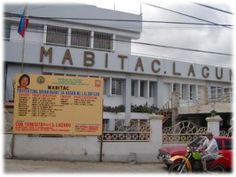 a man riding a motorcycle past a tall white building with a sign on it's side