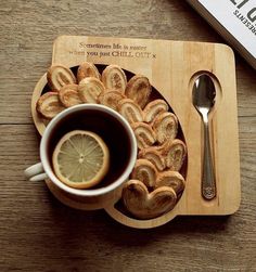 a cup of coffee and some cookies on a wooden tray next to a book with a spoon