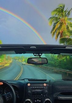 a car driving down a road with a rainbow in the sky and palm trees behind it