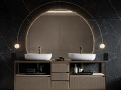 two sinks in front of a round mirror with lights above it and black marble walls