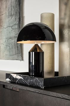 a black lamp sitting on top of a table next to a wall mounted art piece