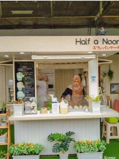 a woman standing behind a white counter in front of plants and potted plants on display